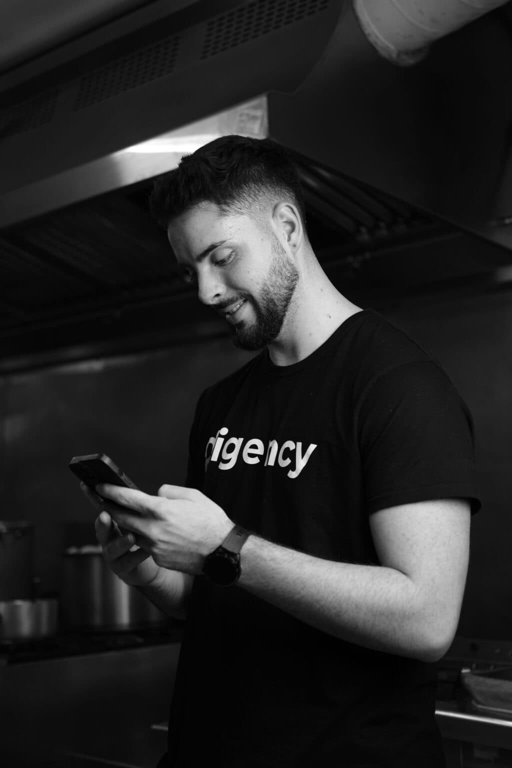 Miembro del equipo de Digency, con camiseta de la agencia, revisando el móvil durante una grabación en la cocina de un cliente