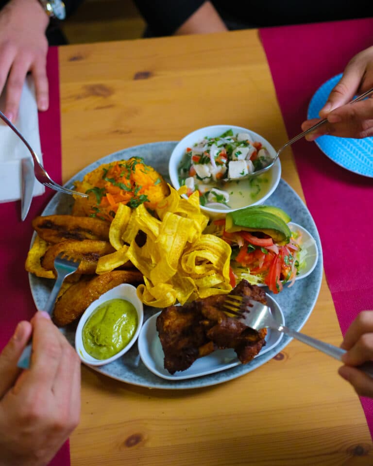 Plato de comida servido en una mesa mientras dos comensales se sirven