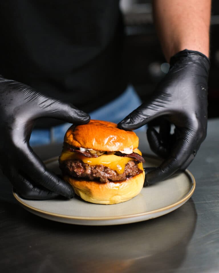 Manos con guante emplatando una hamburguesa en la cocina