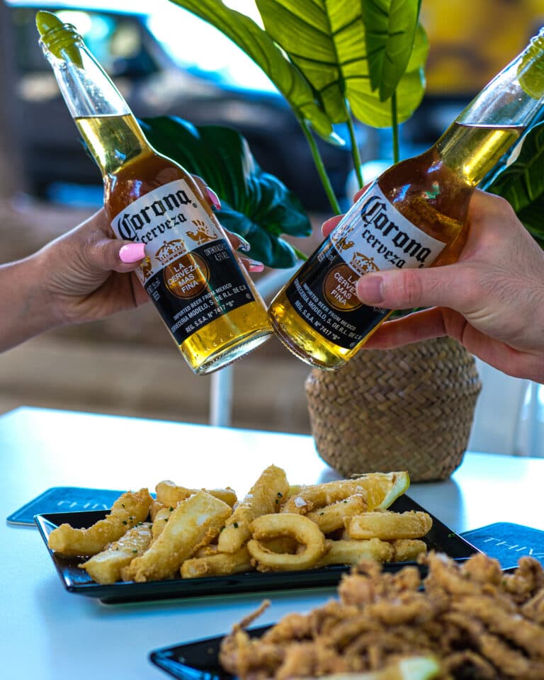 Brindis con dos cervezas sobre una mesa con fritura para compartir